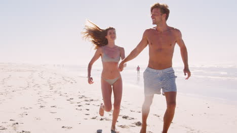 Couple-In-Swimwear-Having-Fun-Running-Along-Summer-Beach-Together