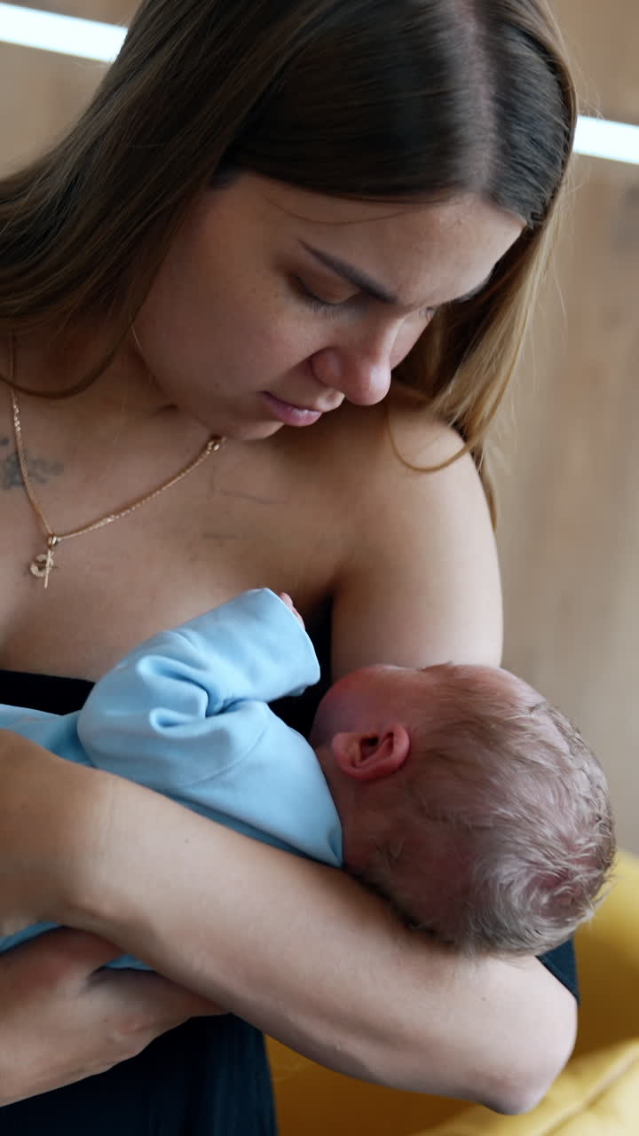 Loving Caucasian mom holding a newborn in hands. Mother is waving the child in blue romper. Vertical video