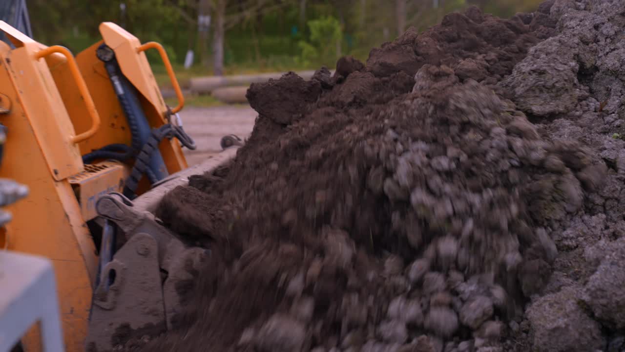 Terreno fertile ricco di nutrienti caricato in un frutteto, con un bobcat che lo versa in una macchina spargitrice trainata da trattore.