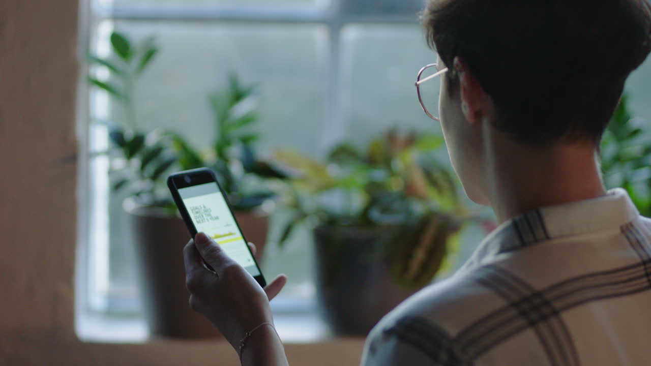 hermosa mujer caucásica usando un teléfono inteligente bebiendo café en casa disfrutando de una mañana relajada navegando por los mensajes de las redes sociales mirando por la ventana enviando mensajes de texto en el teléfono móvil usando gafas