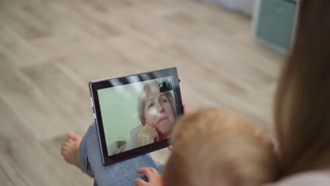 Mom-and-kids-talk-to-grandma-on-video-call-via-modern-tablet