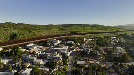 Vista-Aérea-Que-Se-Eleva-Sobre-Las-Casas,-Hacia-El-Muro-Fronterizo-En-El-Soleado-San-Ysidro,-Tijuana,-México