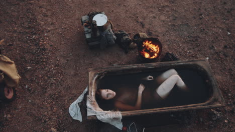 woman bathing in dirty water at post apocalyptic campsite