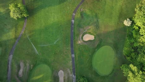 an aerial top down view of a well maintained golf course in queens, new york during a sunny morning while the sprinkler system is turned on