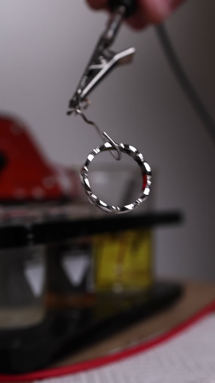 Primo piano di un anello d'argento tenuto da una pinza metallica