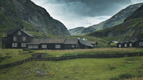 traditional wooden buildings sit in a green boverdalen valley, surrounded by towering mountains and rocky slopes