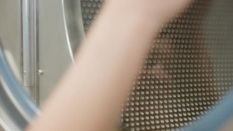 Close up hand view of laundry attendant wiping transparent surface door of washing machine with soapy towel, leaving streaks of water and reflection visible on glass while performing cleaning task