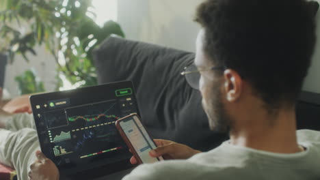 man trading online with laptop and phone at home