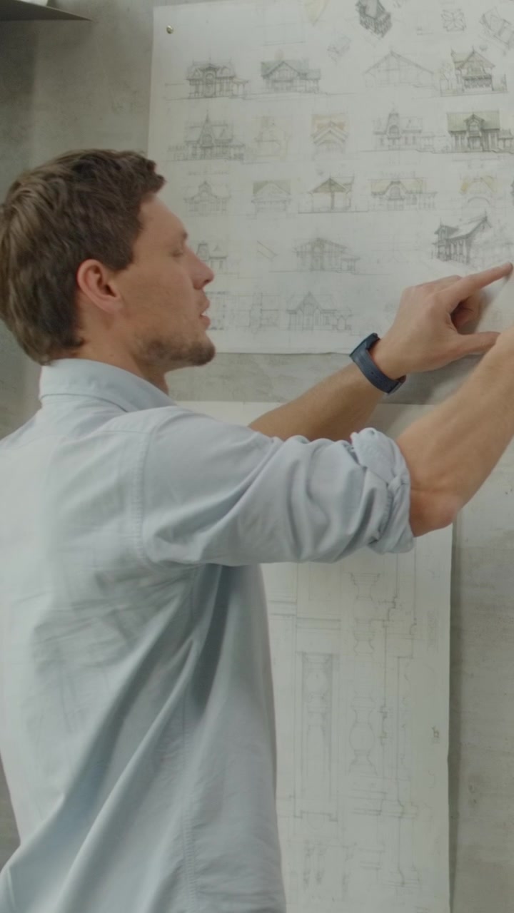 Architect Pinning Architectural Drawings to Wall in Office