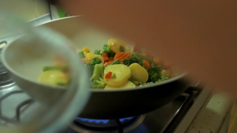 cooking and mixing frozen vegetables in a white frying pan, making healthy vegetarian food, steam coming up, closeup handheld shot