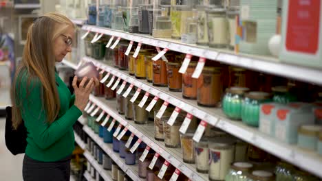 Plano-General-De-Una-Mujer-Rubia,-Bonita-Y-Madura-Mirando-Velas-Y-Oliéndolas-En-La-Exhibición-De-Una-Tienda