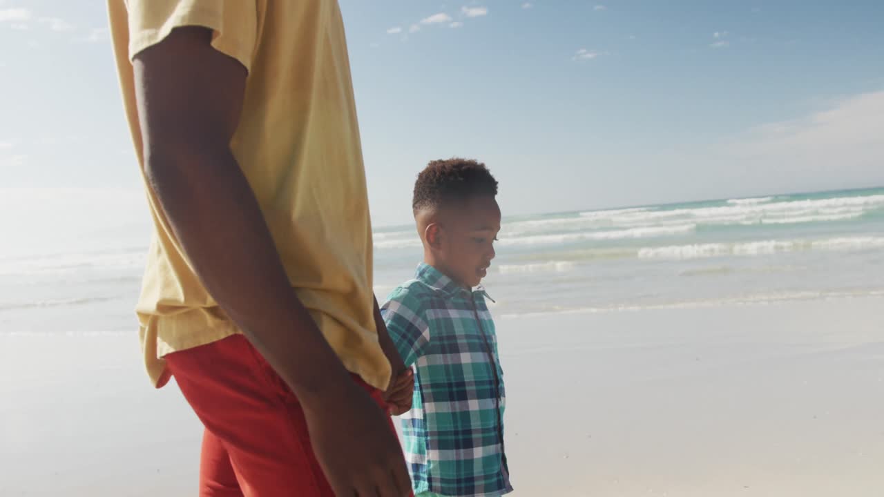African american son holding his father's hand while walking on the beach
