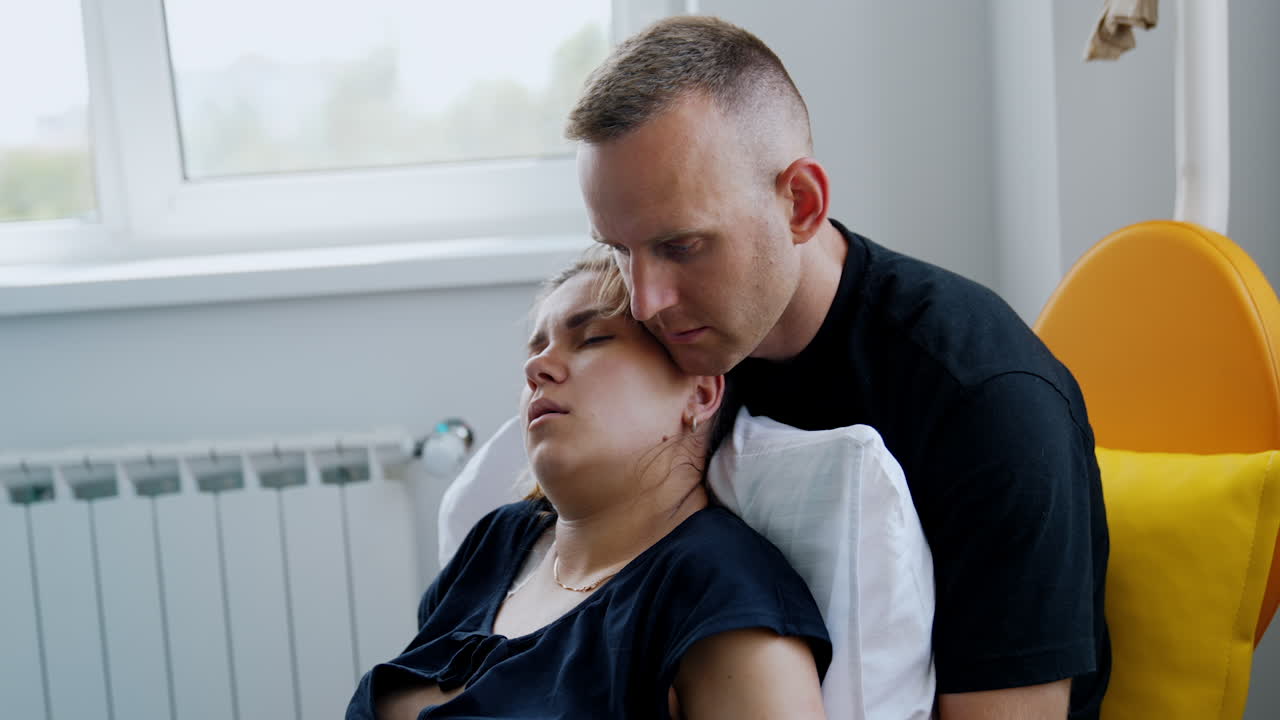 Exhausted Caucasian woman lies in her husband's arms. Pregnant lady is tired from painful contractions.