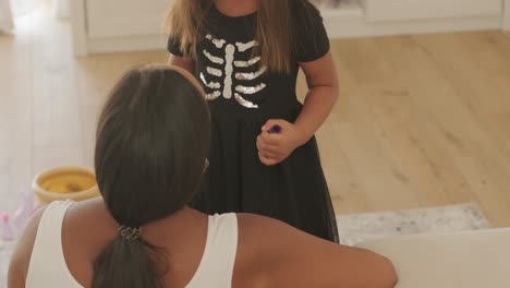niña con sombrero de bruja aplicando maquillaje a su madre embarazada para halloween