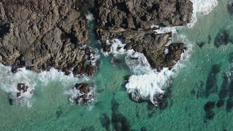 waves crash against the ancient volcanic rock protruding into the warm tropical waters of the pacific ocean