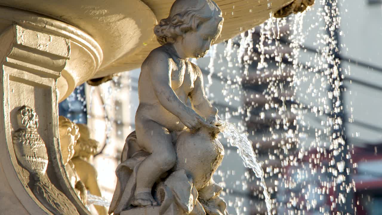 La luce del sole illumina l'acqua che zampilla da una statua di cherubino in pietra presso la storica Fontana Carriedo.