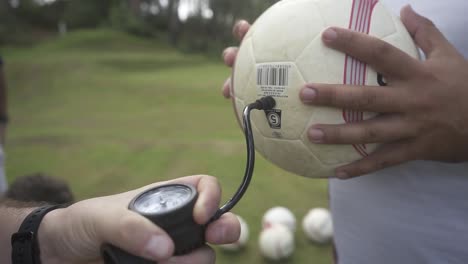 soccer coach carefully preparing soccer ball, using hand pump to inflate and verify pressure before match on sunlit grassy field