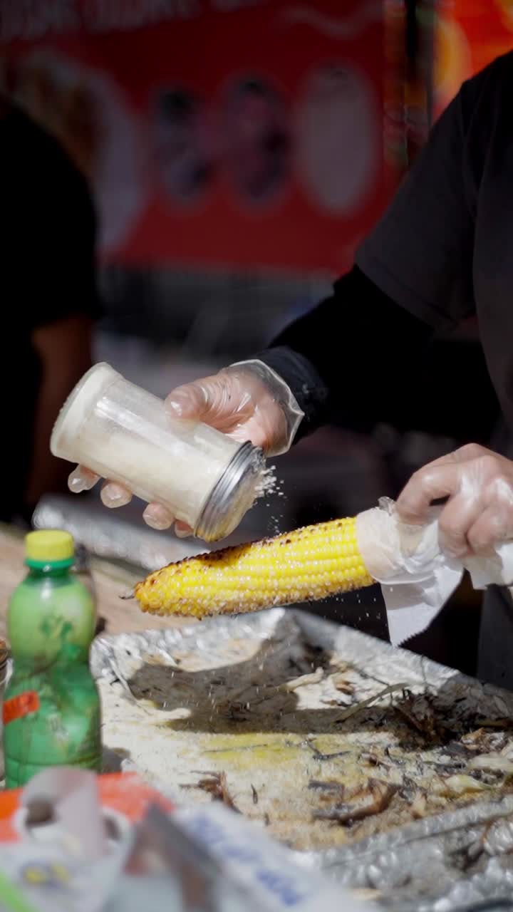 Slow motion view of a cooker preparing a Mexican corn Elote with cheese in a street food market.