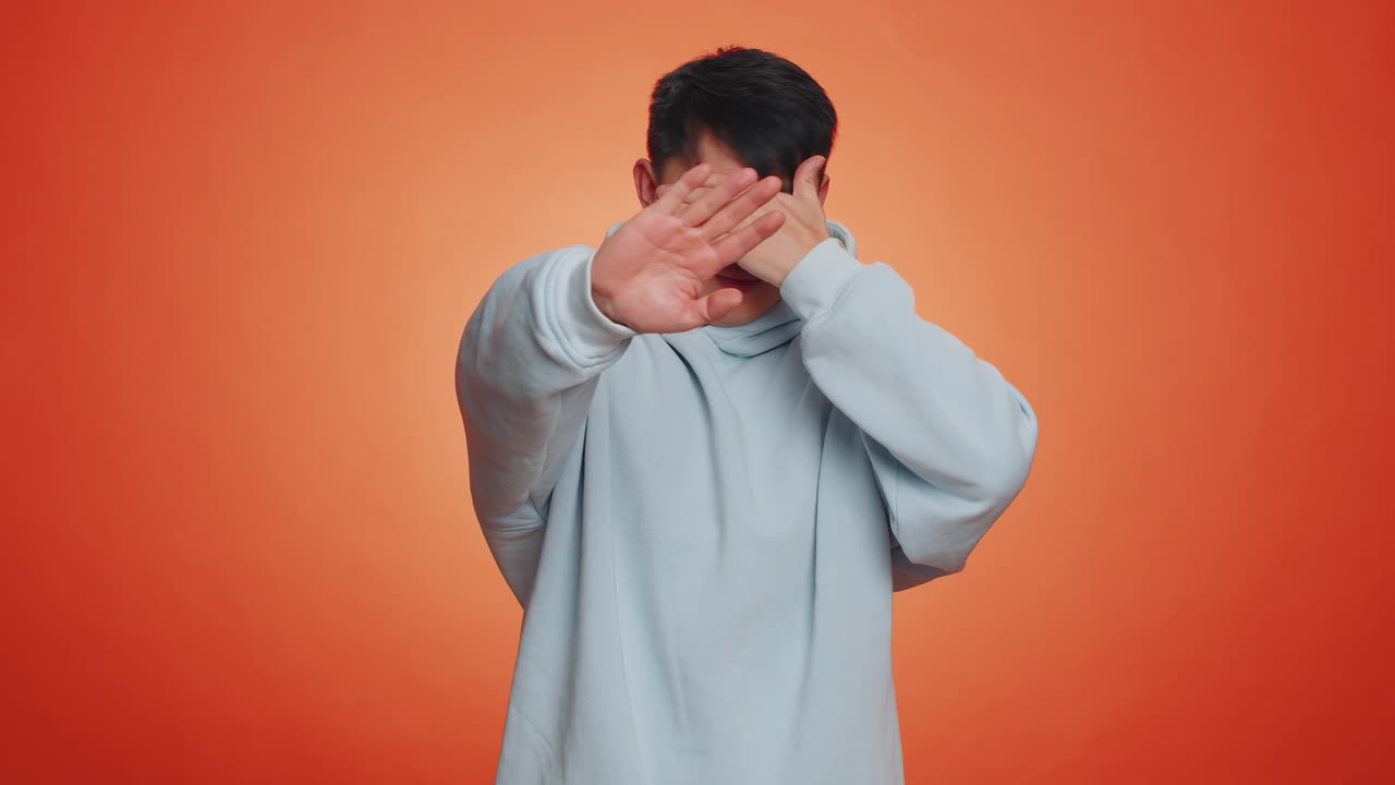 Afraid asian man closing eyes with hand showing stop gesture confused shy scared to watch awful