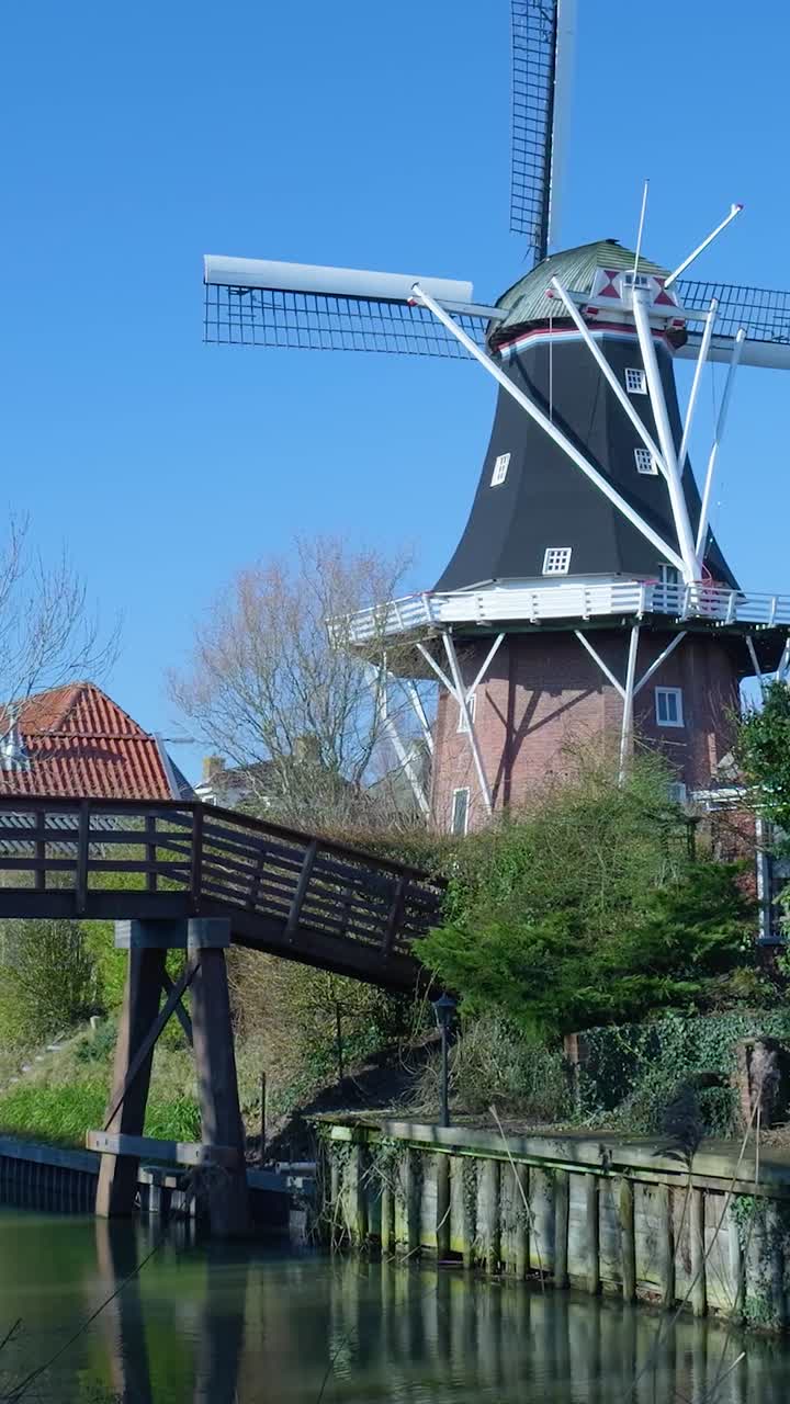 Mulino a vento tradizionale olandese e ponte di legno su un canale.