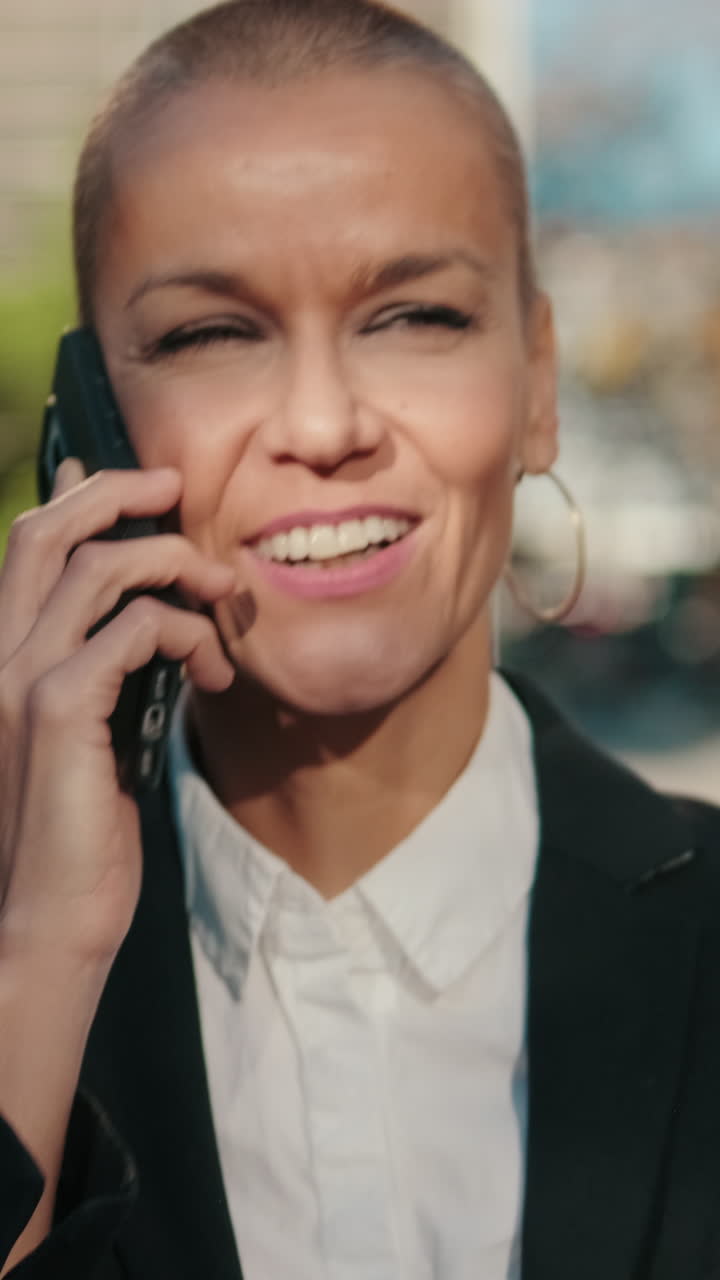 Mulher de negócios confiante falando ao smartphone e sorrindo ao ar livre