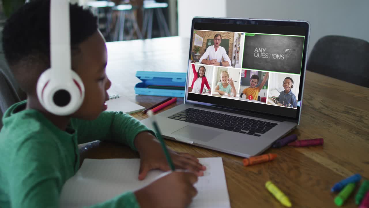 Schoolboy using laptop for online lesson at home, with diverse teacher and class on screen