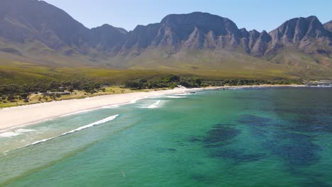 white sand beach with kogelberg mountain ridge in the background of a calm green looking atlantic ocean in kogel bay