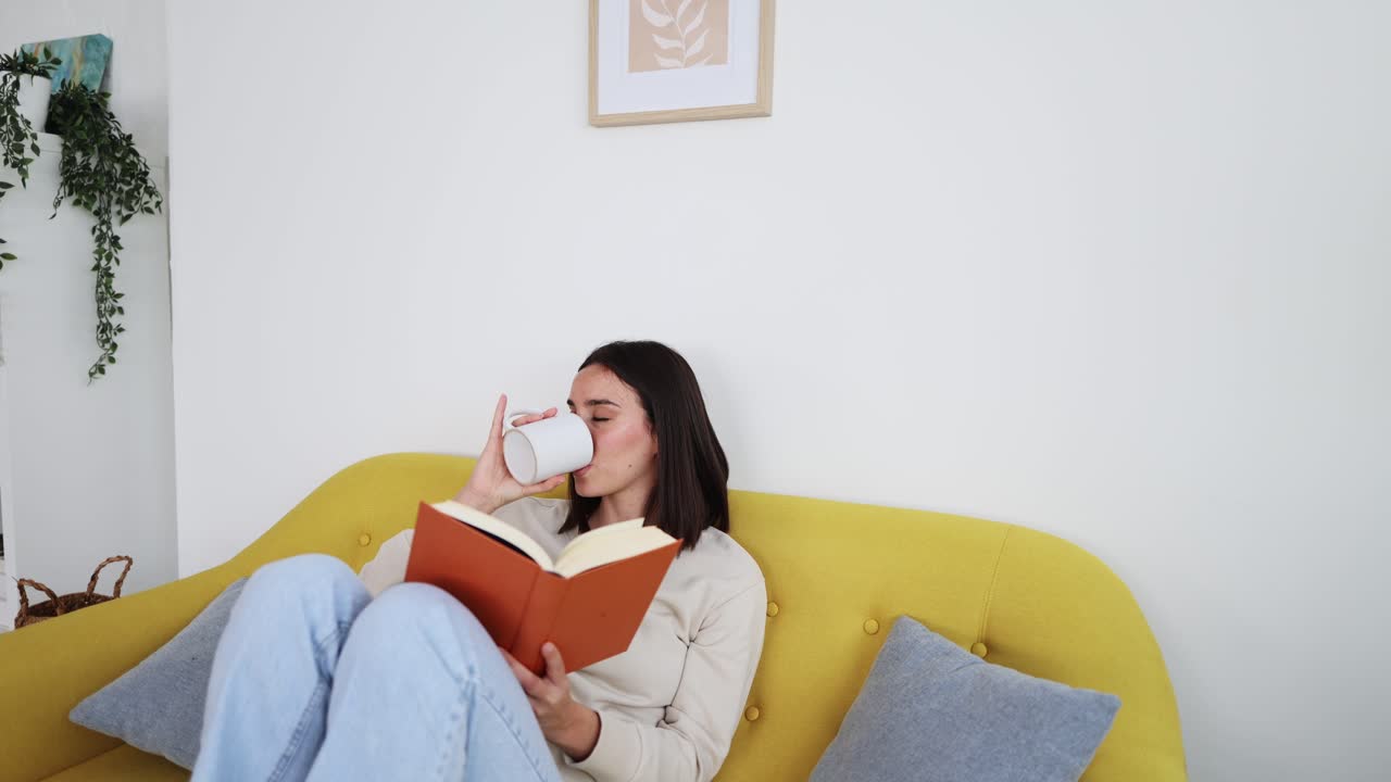 ソファでくつろぎながら本を読み、コーヒーを飲む若い女性