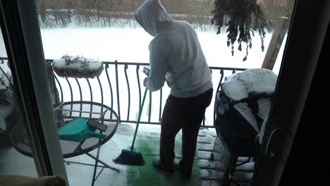 a guy cleaning his balcony floor from accumulated snow