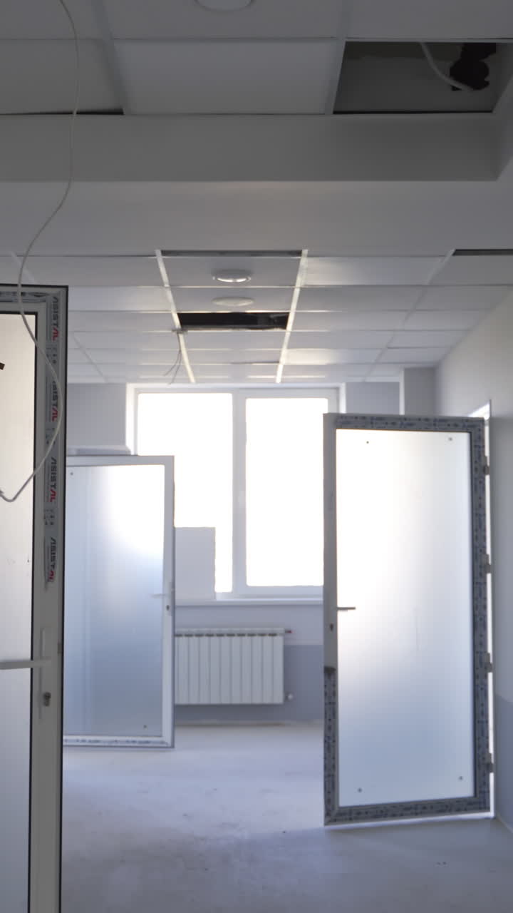 White corridor in a newly-built building. Focus on the unfinished pieces of ceiling cover. Open doors lock close up. Vertical video