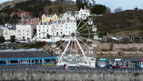 Llandudno-pier-Victorian-promenade-Ferris-wheel-attraction-and-Grand-hotel-resort-aerial-view-slow-right-orbit-shot