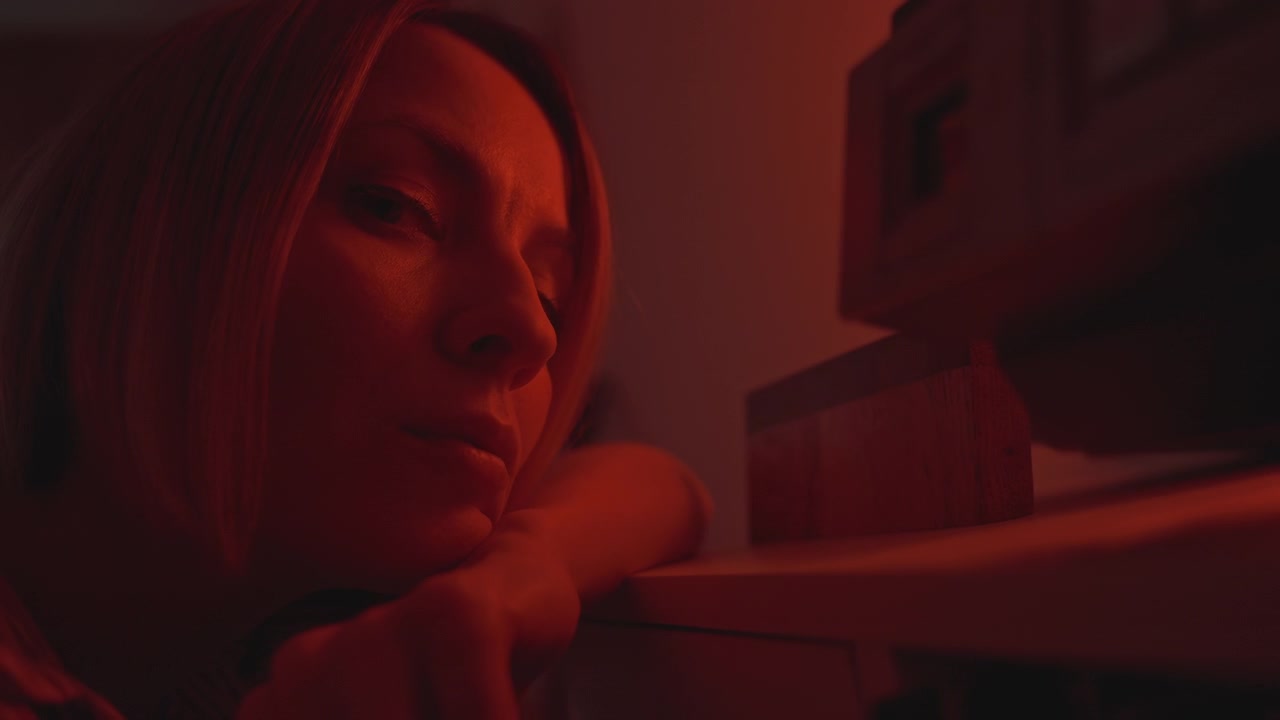 Donna caucasica pensierosa alla tastiera sotto una luce rossa da studio, sessione di composizione a tarda notte, primo piano di profilo che si appoggia al pianoforte mentre riflette, grana cinematografica, ombre a bassa chiave, atmosfera intima e malinconica
