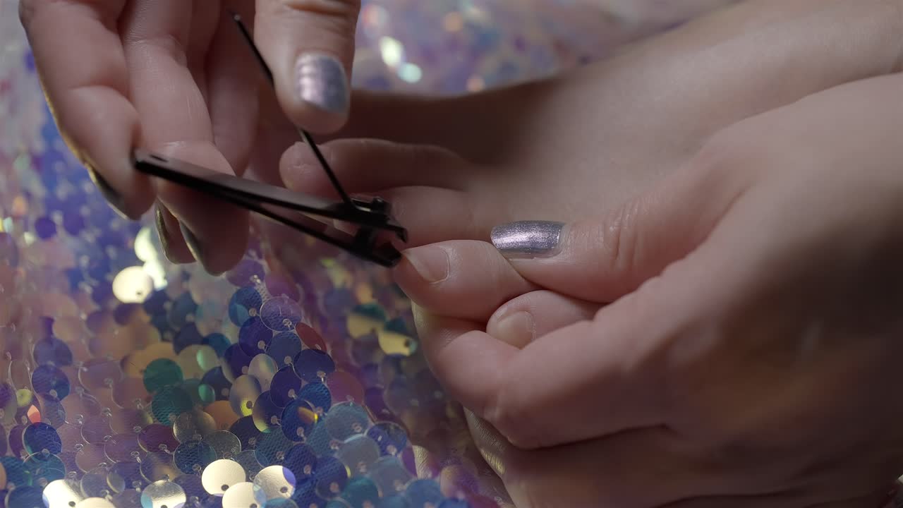 Side view in 4K slow motion of woman trimming toenails above sequin fabric
