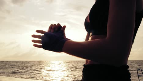 Close-Up-view-of-woman-getting-her-fists-ready-for-the-boxing-gloves-by-wrapping-bandage-around-them-standing-against-the-son