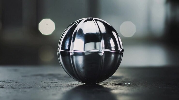 Pushing camera metal sphere shifting highlights on tabletop studio revealing welded seam and bokeh