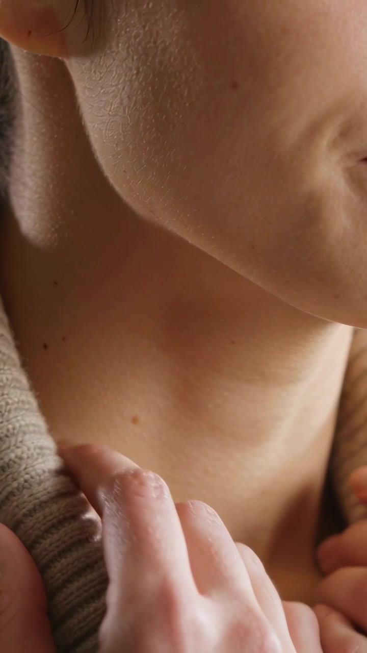 Video verticale: Mano che tira il colletto di un maglione beige a casa, regolando la vestibilità ed esponendo la mascella.