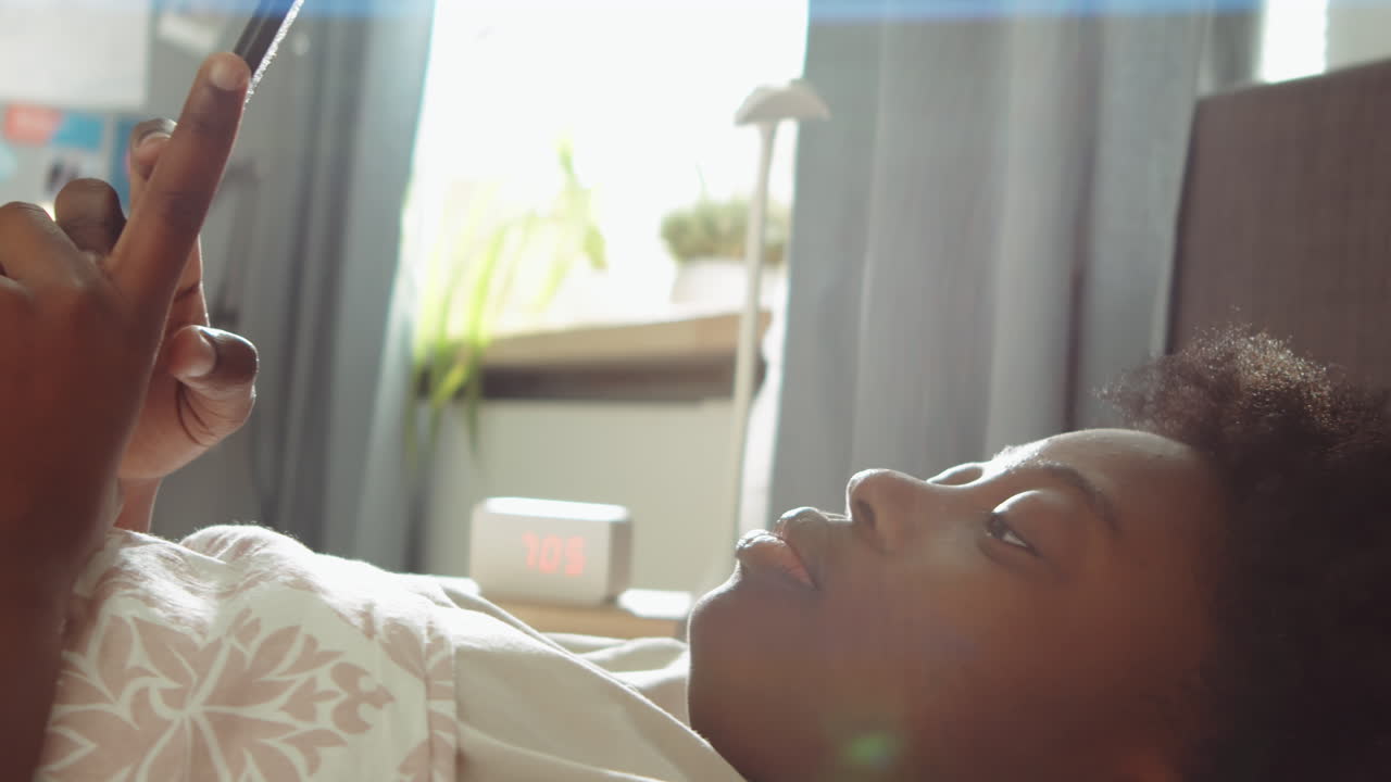 Donna afroamericana sdraiata a letto che usa il telefono