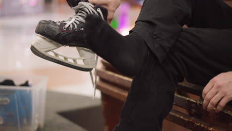 a close view of someone with a black ice skating shoe wearing black socks, as he dangle his leg, with blue skating shoe in a container by the side