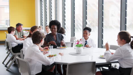 Lehrerin-Mit-Einer-Gruppe-Von-Gymnasiasten-In-Uniform,-Die-Am-Tisch-Sitzt-Und-In-Der-Cafeteria-Zu-Mittag-Isst