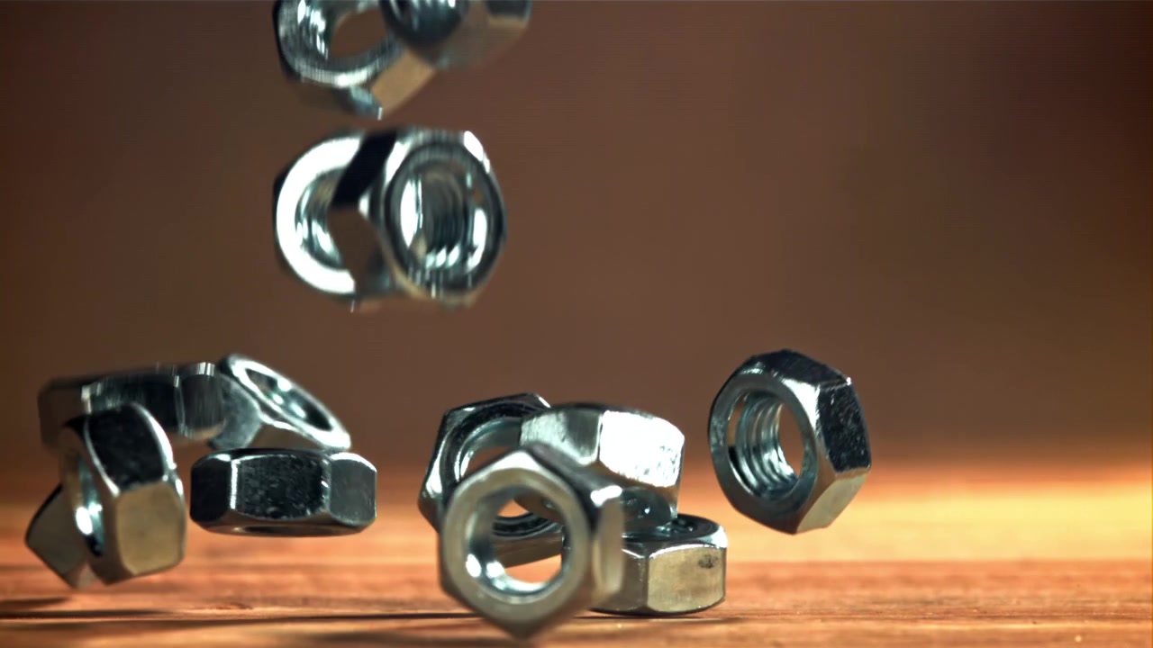 Skinnende metalmøtrikker falder og spredes i slow motion