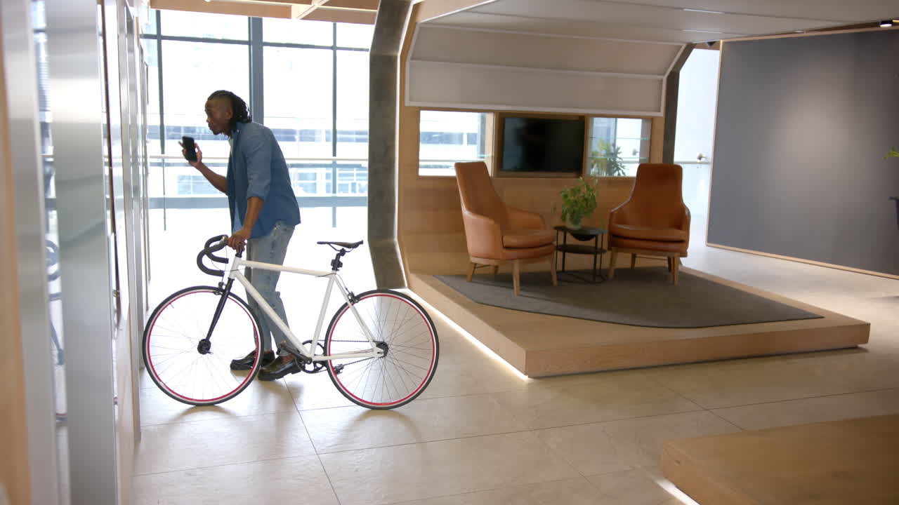 Talking on smartphone, man with bicycle standing in modern office lobby, copy space