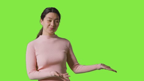 portrait of woman presenting or demonstrating item against green screen smiling at camera