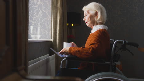 Senior-Woman-In-Wheelchair-With-Energy-Bill-By-Radiator-In-Cost-Of-Living-Energy-Crisis