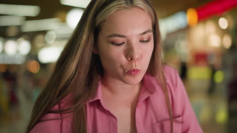 lady in pink dress takes a bite of burger, chewing slowly, nodding her head with satisfaction due to the delicious taste. she appears thoughtful while savoring the food, with a blurred background