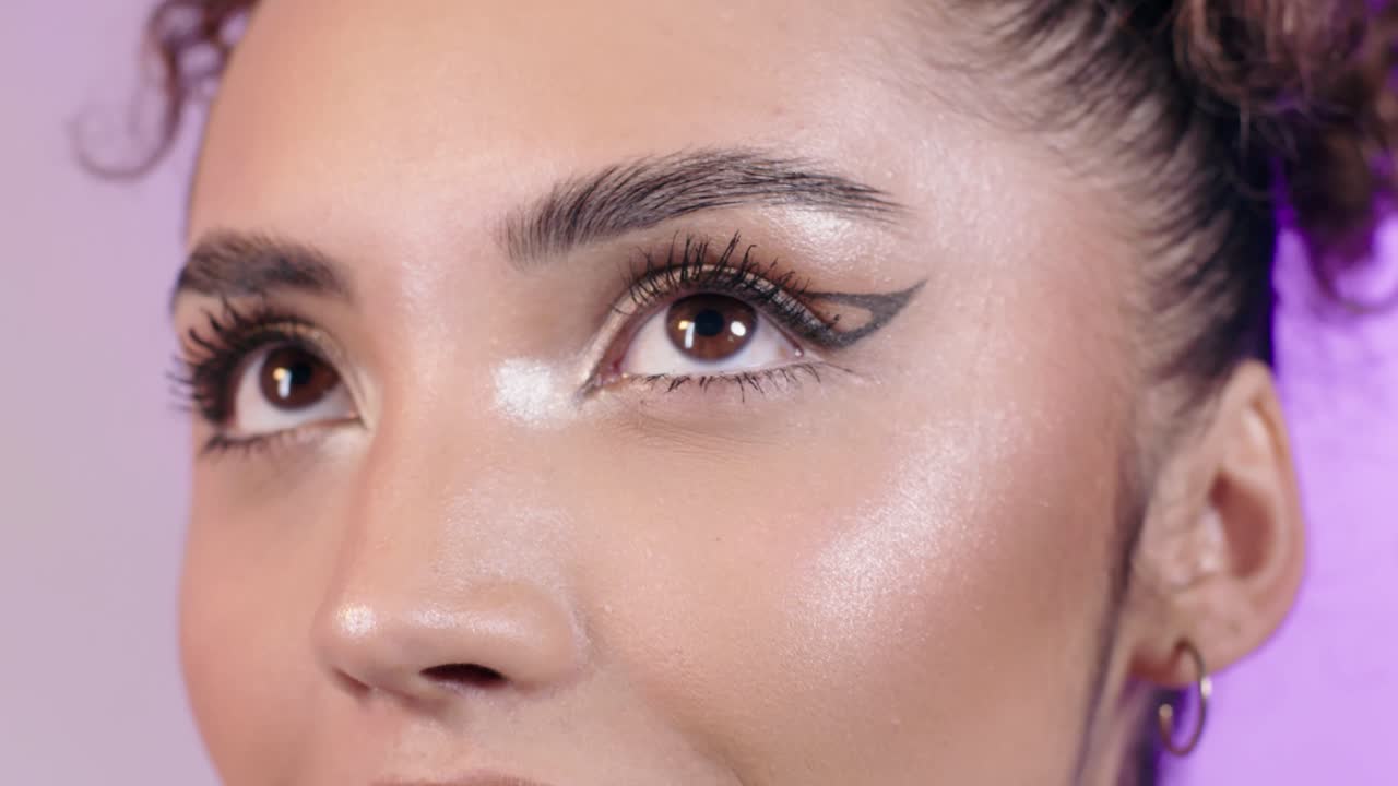 Close up of a beautiful young woman smiling and applying highligher with her fingers on her eye inner corner, make up, cosmetics, on a pink background