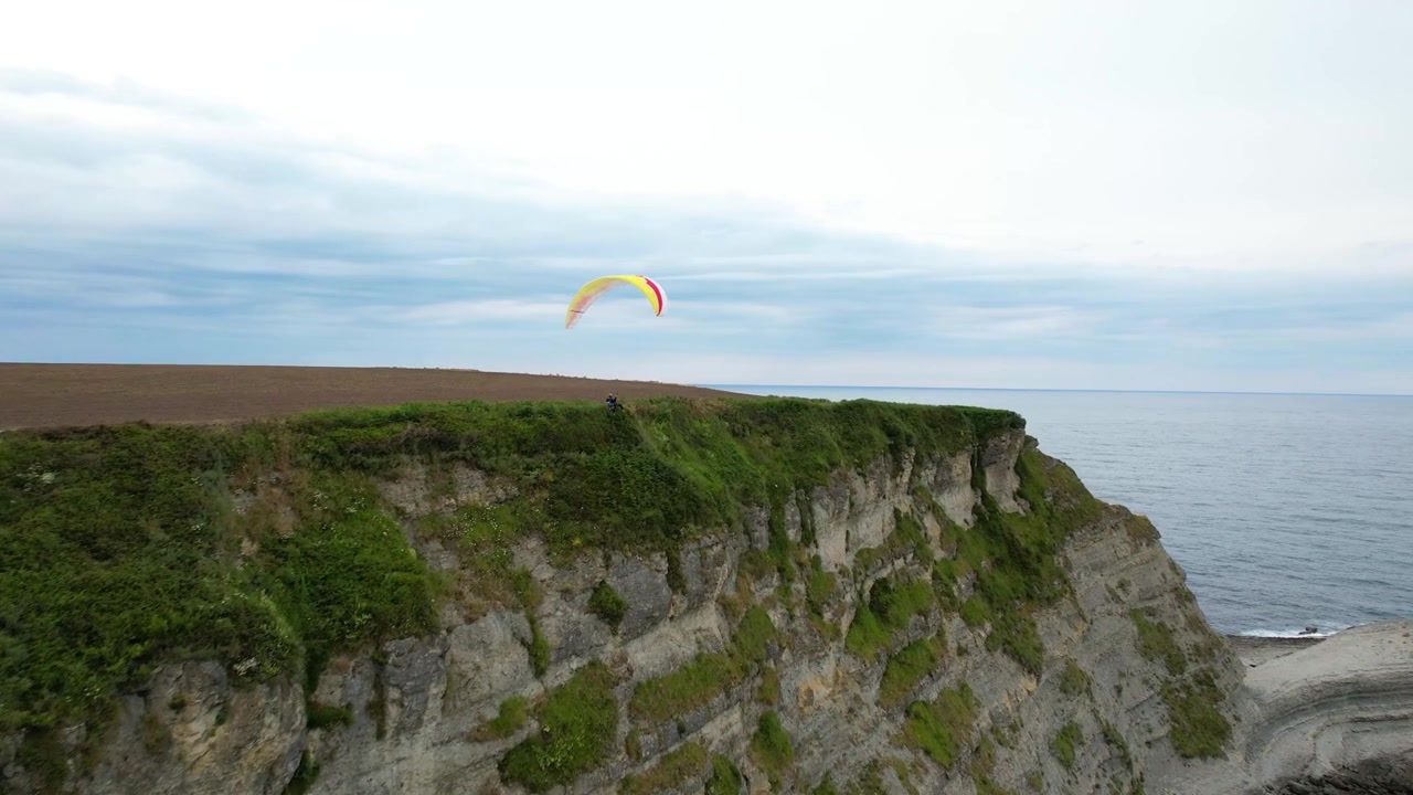 Parapente sobre acantilados costeros con vistas al océano.