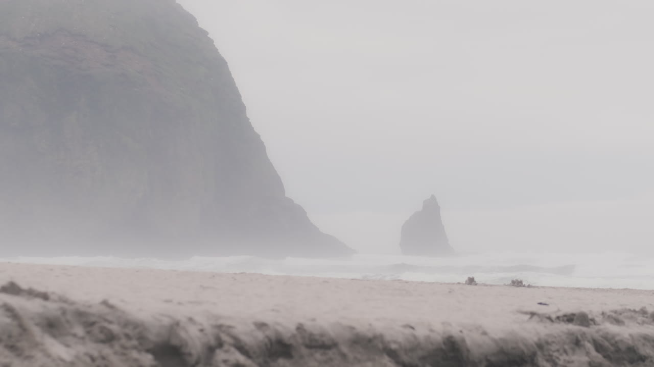 la niebla pasa por la roca del pajar en la costa de oregon en un día de mal humor mientras las olas rompen en la orilla