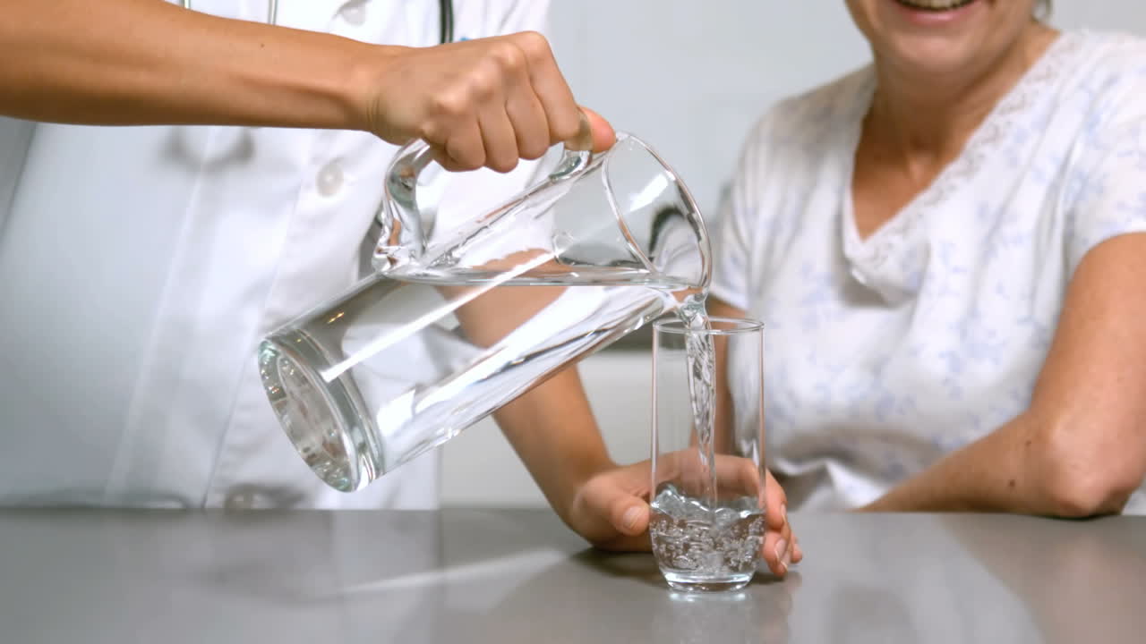 enfermera en el hogar vertiendo agua para el paciente en la cocina