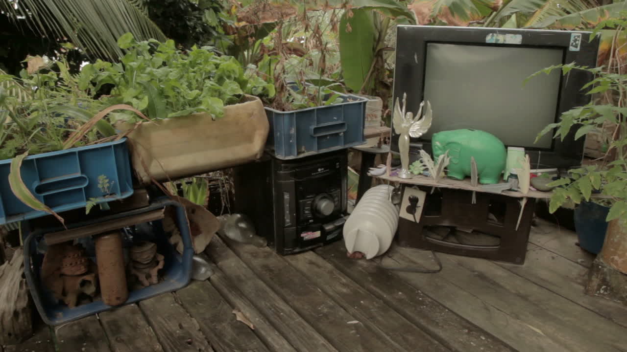 Wide shot of decorative waste with broken tv, stereo and plants at a Darien Gap rustic house in Colombia.