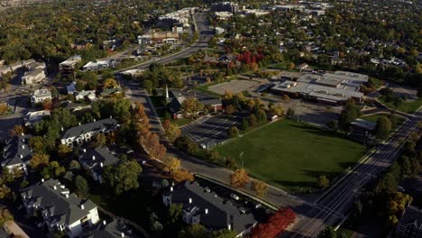 Tilt-up-dolly-in-aerial-drone-wide-landscape-shot-revealing-the-stunning-snowcapped-rocky-mountains-of-Utah-with-Salt-Lake-county-below-full-of-buildings-and-colorful-trees-on-a-warm-sunny-fall-day